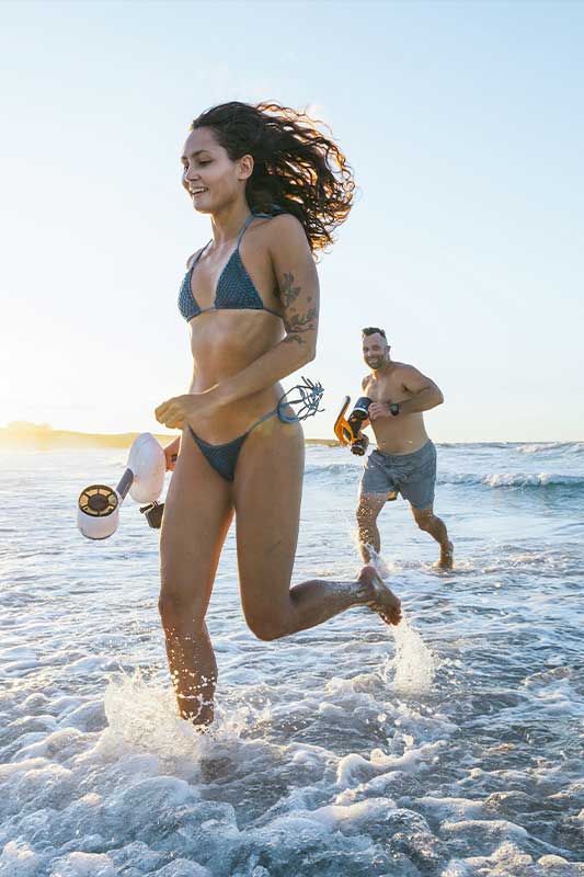 couple qui court sur la plage au bord de l'eau avec un scooter sous marin sublue