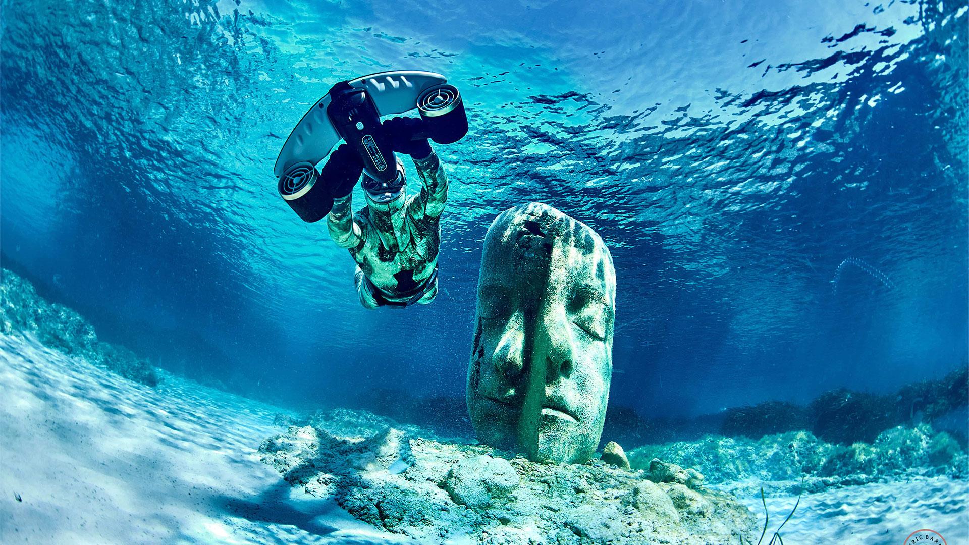 nage a coté d'une statue maya au fond de l'eau avec un scooter sous marin sublue