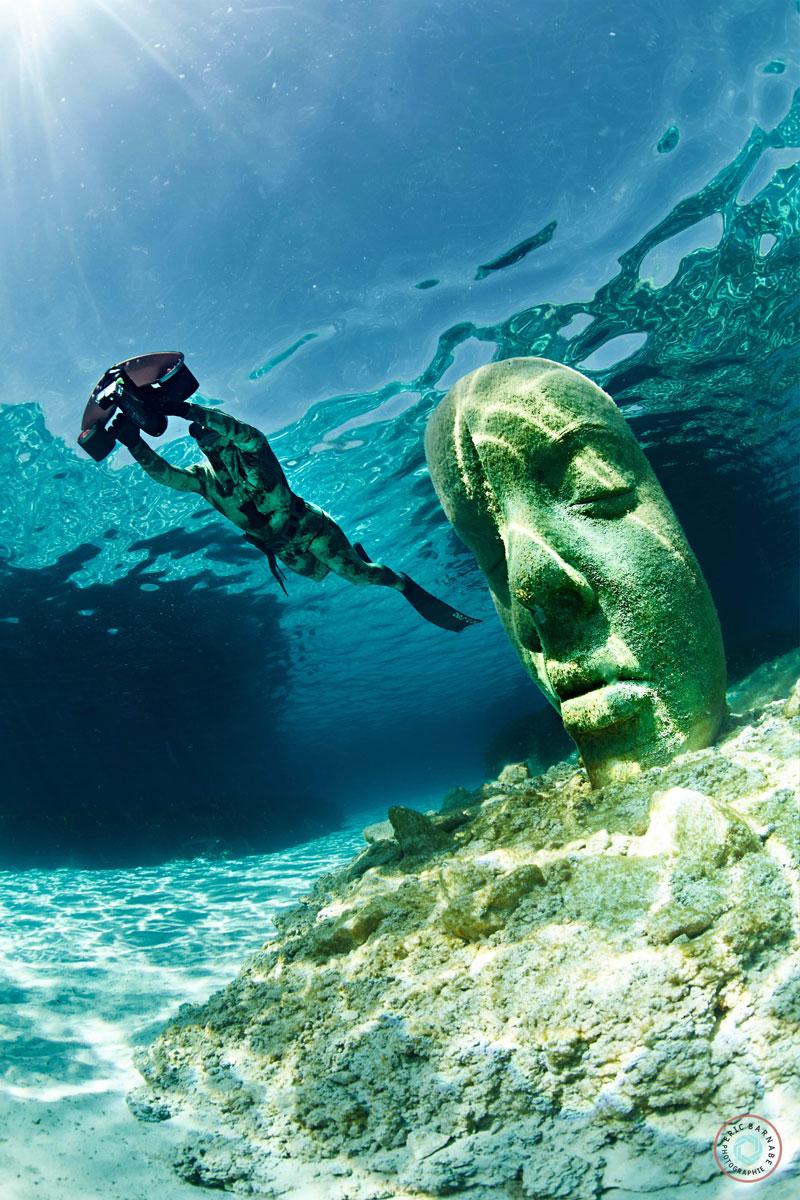 statue visage avec un plongeur a coté qui glisse sous l'eau avec un scooter sous marin sublue