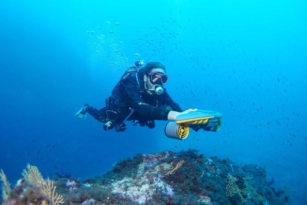 un plgoneur avec un scooter sous marin sublue navbow proche de roche magnifique sous l'eau