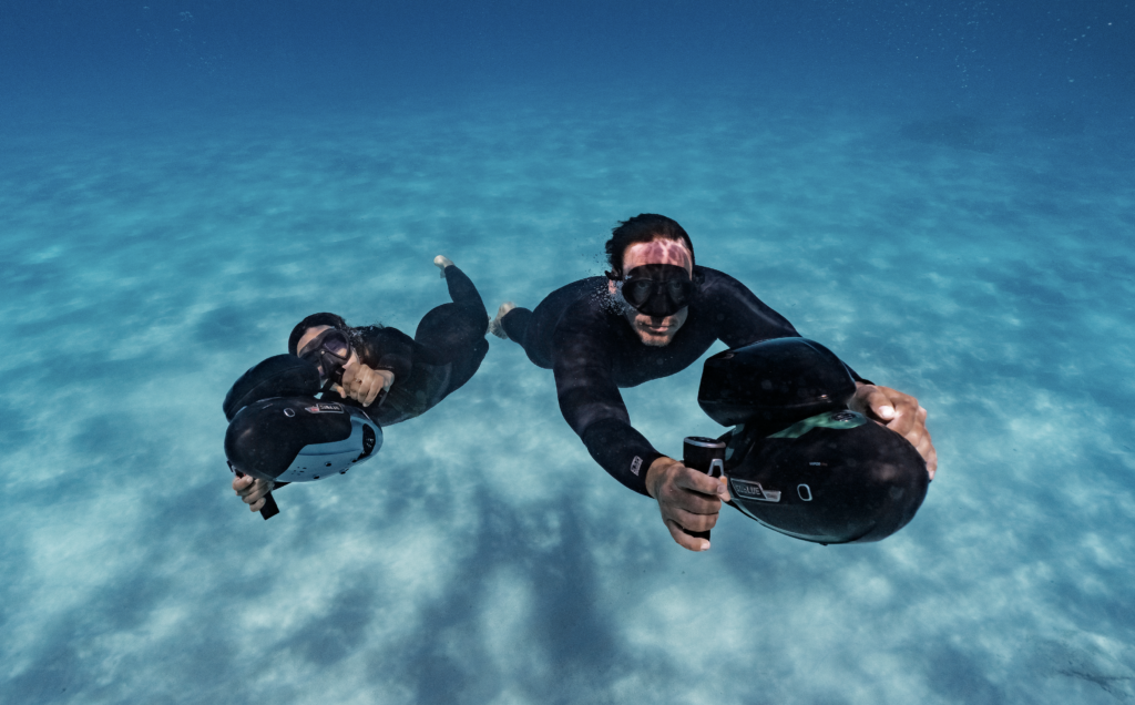 Two divers over a sandy bottom with Sublue Vapor Pro scooters
